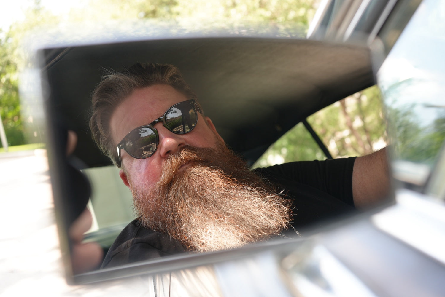 Comedian Jerry Wayne Longmire, full beard and sunglasses, reflected in a car mirror — Outlaws & Gents brand partner