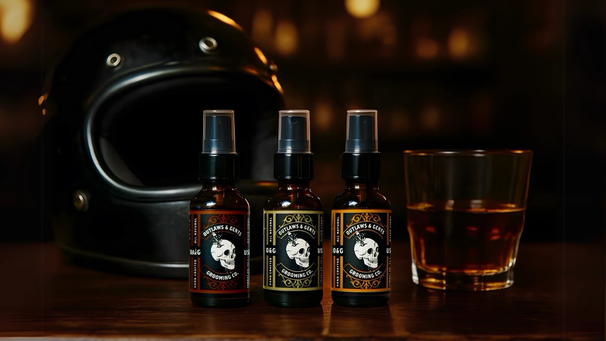 Trio of Outlaws and Gents beard oils on wooden surface with whiskey glass and metal skull blurred in background