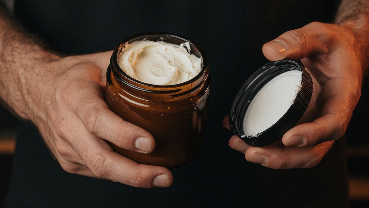 Fingertips scooping whipped beard butter from an amber jar — beard butter as a deep-conditioning men's skin moisturizer