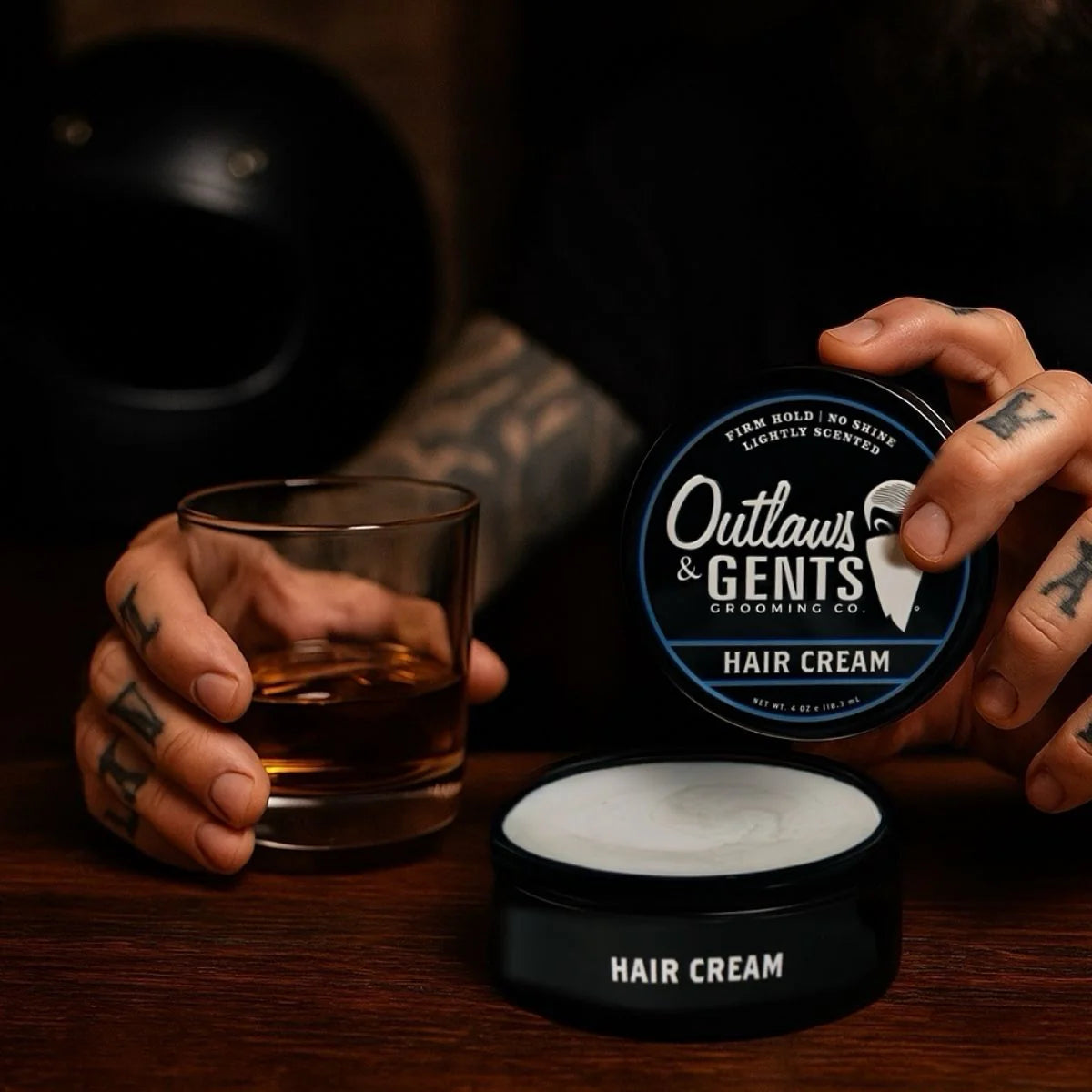 Tattooed hands with Outlaws and Gents hair cream and glass of whiskey 